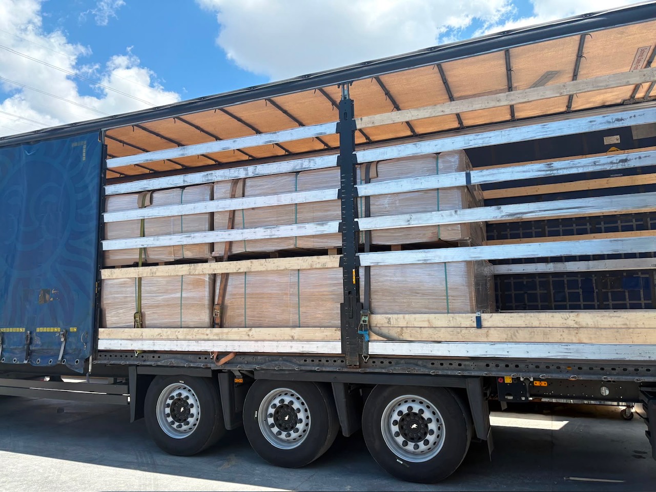 Side view of a curtain-side truck loaded with stacked pallets of acoustic wall panels